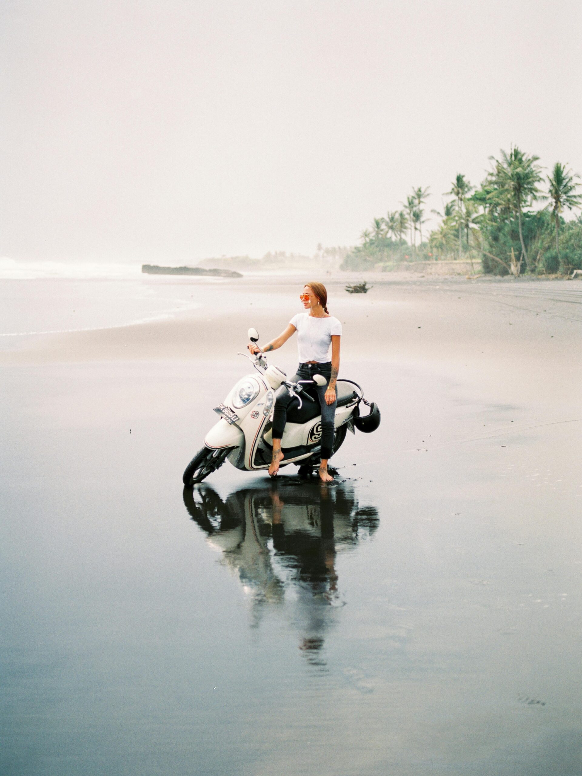 A woman on a scooter enjoys a serene beach view in Bali.