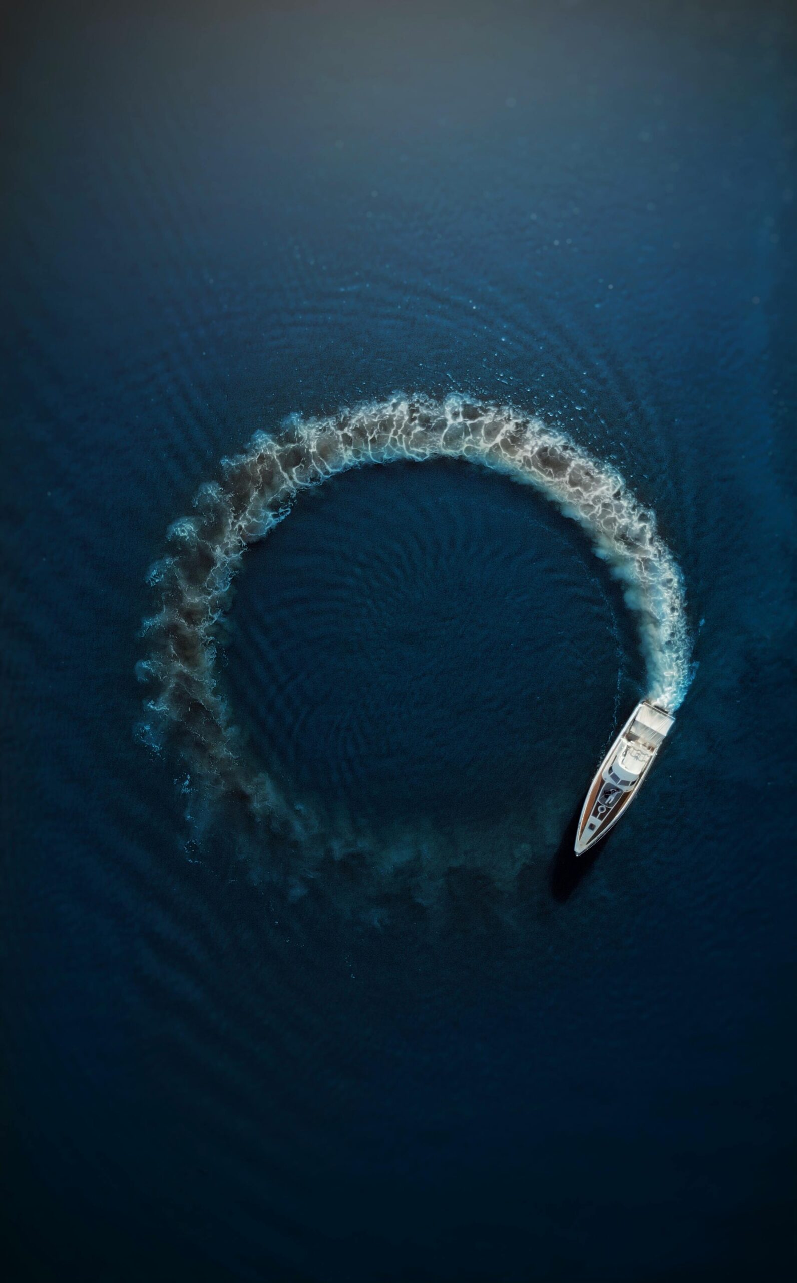 An aerial shot of a motorboat making a circular ripple pattern in the azure ocean water, showcasing motion and summer vibes.